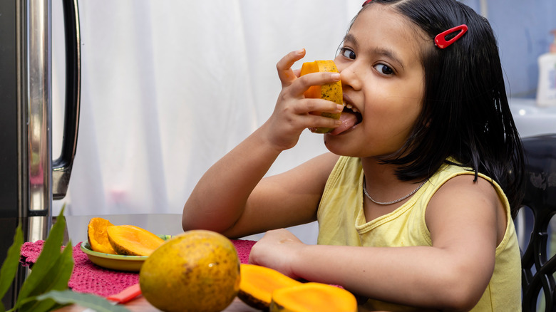 a young girl eating mangoes