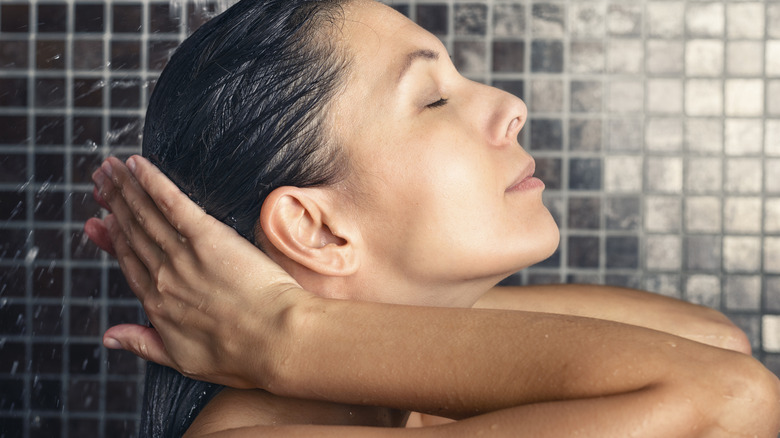 Woman with closed eyes rinsing out wet hair in shower