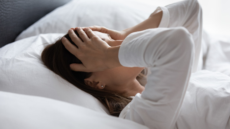 woman in bed holding her head in pain