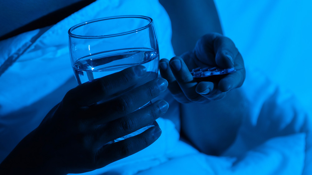 Woman holding glass of water and pills in the dark 