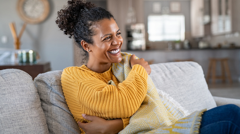 Woman sitting on couch under blanket, laughing