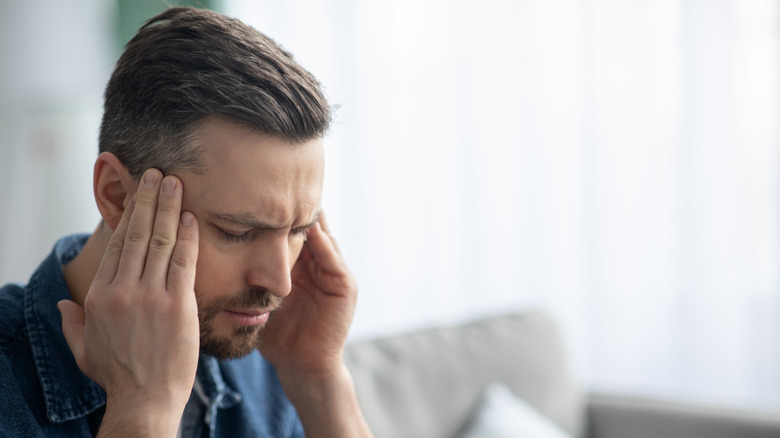 Closeup of bearded man suffering from headache at home, touching his temples