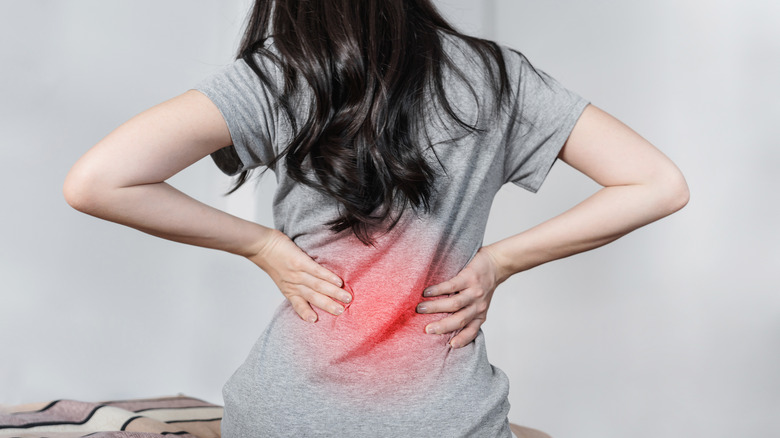 Young woman sitting on bed after waking up, holding her lower back with redness on it