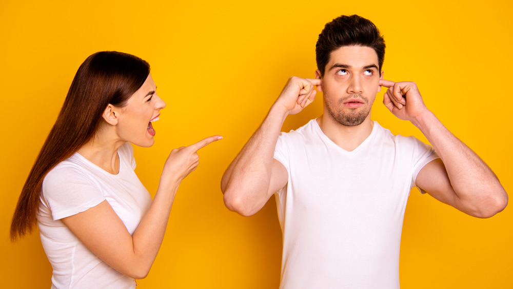 man plugging ears while being yelled at by woman