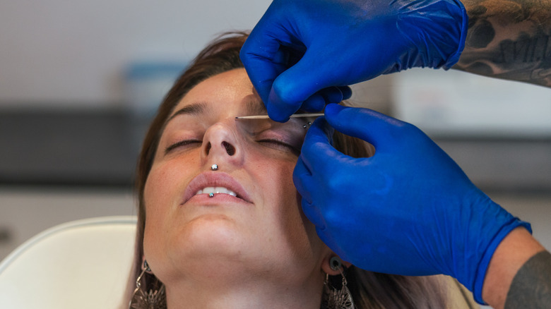 Woman receiving facial piercing