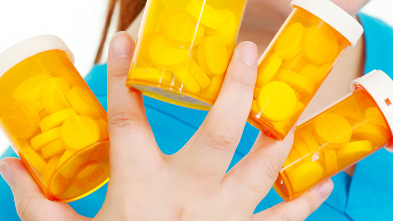 Woman's hand holding pill bottles between fingers