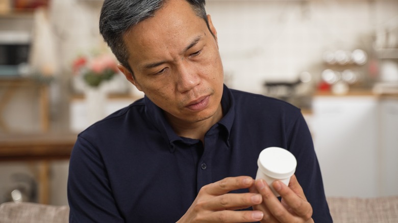 Asian older man peering at pill bottle and looking confused