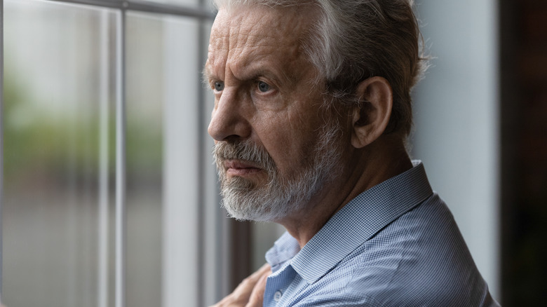 Worried older man looking out window of home