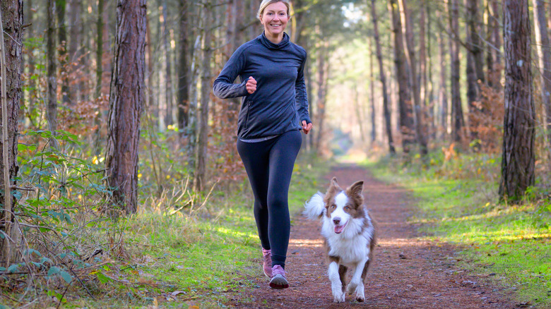Young woman jogging on forest path with dog