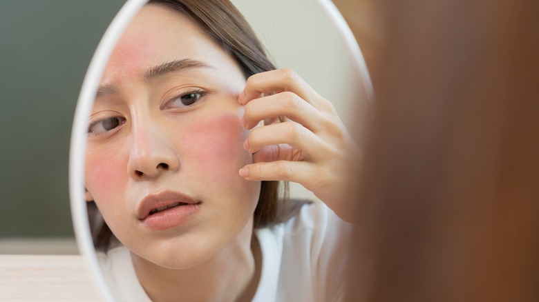 woman examining irritated skin in mirror