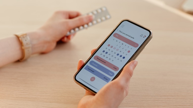 woman holding birth control pills and using menstrual cycle app