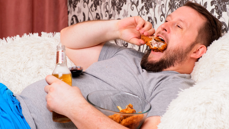 man with beer and fried chicken on couch