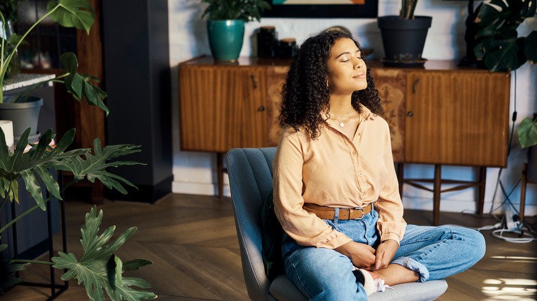 woman meditating indoors surrounded by plants