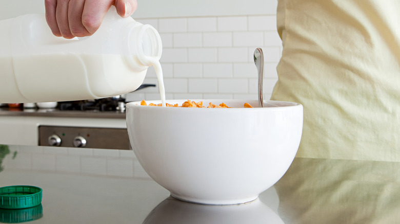 person pouring milk into cereal bowl