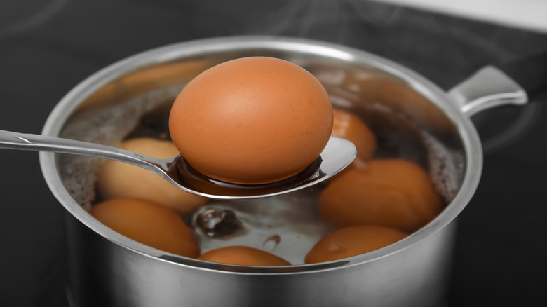 Spoon with boiled egg above saucepan