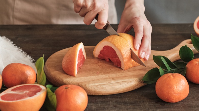 Woman slicing grapefruit on wooden board