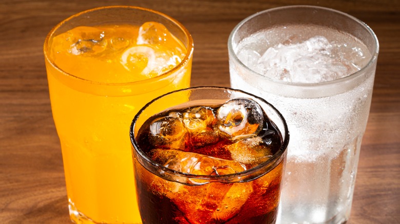 glasses of soda, orange soda, and clear soda on a counter