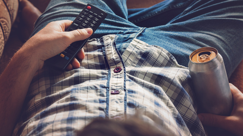 Man laying on couch with beverage and TV remote