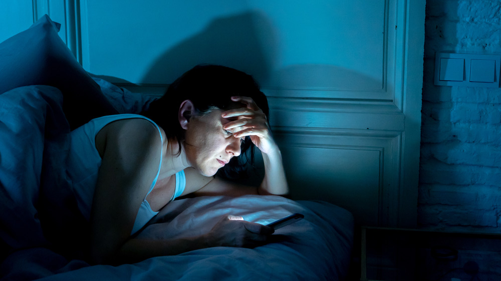 Woman looks at smartphone in bed