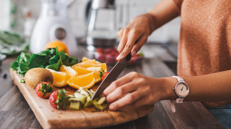 woman in kitchen cutting fruit next to blender