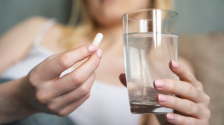 A woman holds a pill and a glass of water