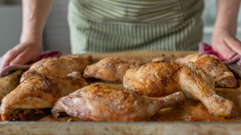 woman behind cooked baked chicken parts in kitchen