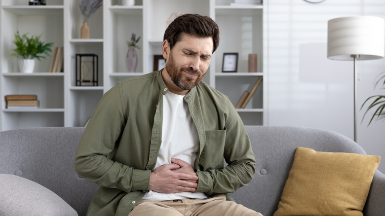 man experiencing stomach pain while sitting on couch