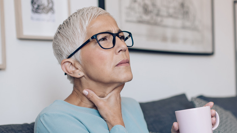 Bespectacled woman looking distressed holding throat