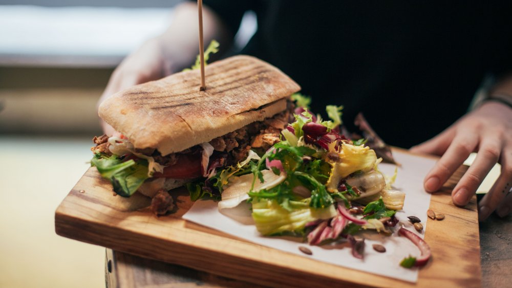 A person's hands holding a large plate with a sandwich and salad