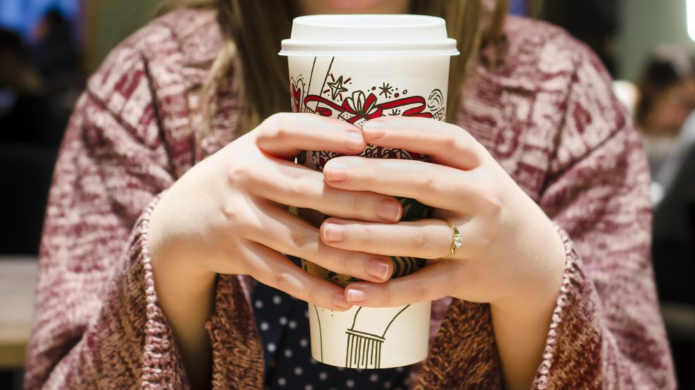 A woman holding a hot coffee beverage