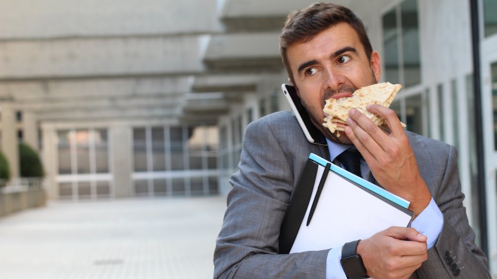 A man eating a sandwich while on his phone, walking