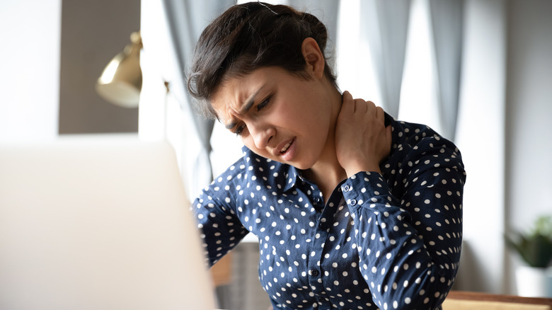 Woman in polka dot shirt grimacing with hand on side of her neck