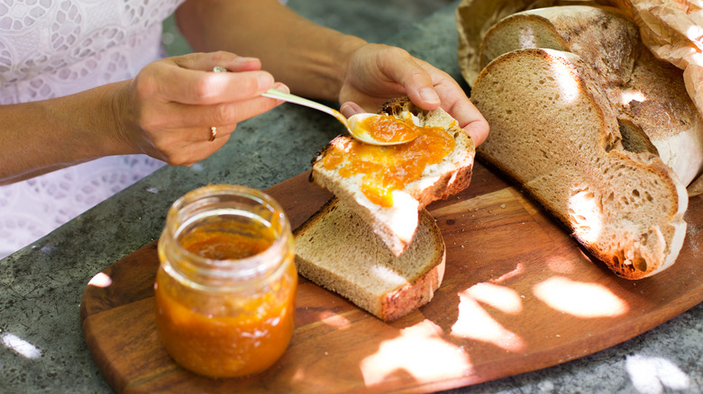 A woman's hands spreading jam over sourdough bread