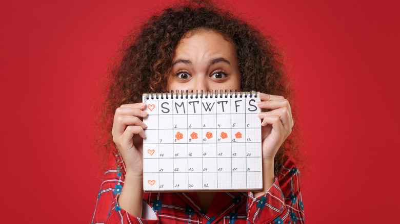 Girl holding calendar over half her face with bleeding days marked