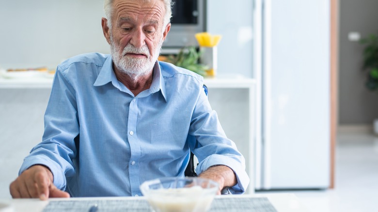 Elderly man stares at bowl of rice