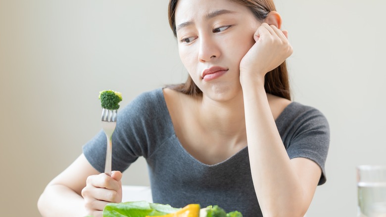 Young woman looks sadly at broccoli