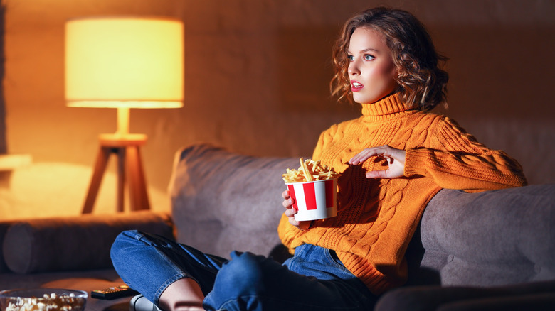 woman watches TV while eating fries