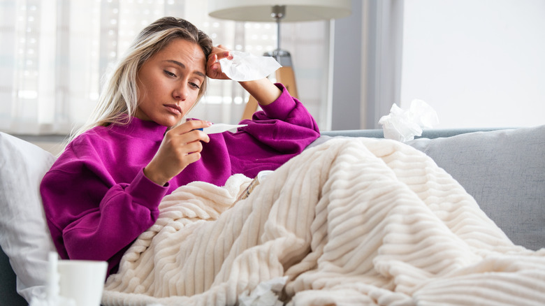 sad woman with blanket holding thermometer 