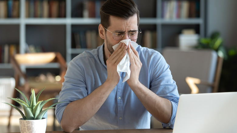 sneezing man sitting at desk