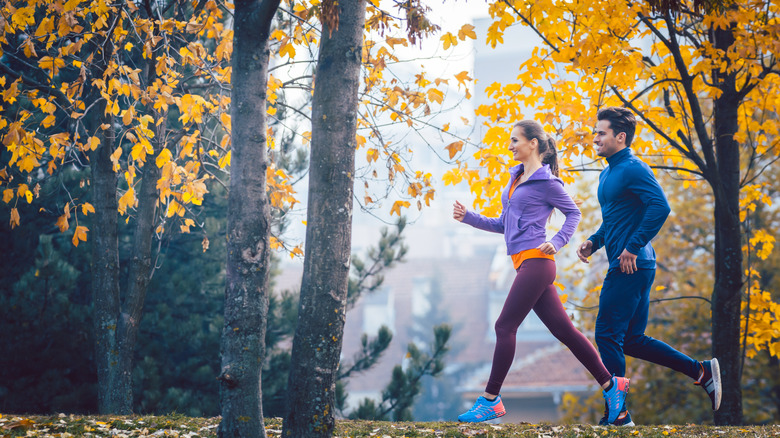 man and woman running in autumn forest