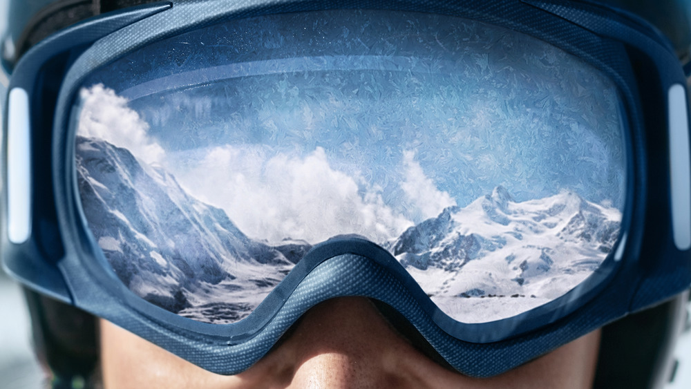 close up of ski goggles with snow covered mountains in the reflection