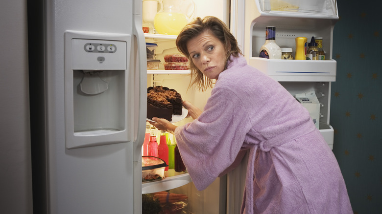 Woman sneaking cake out of refrigerator 