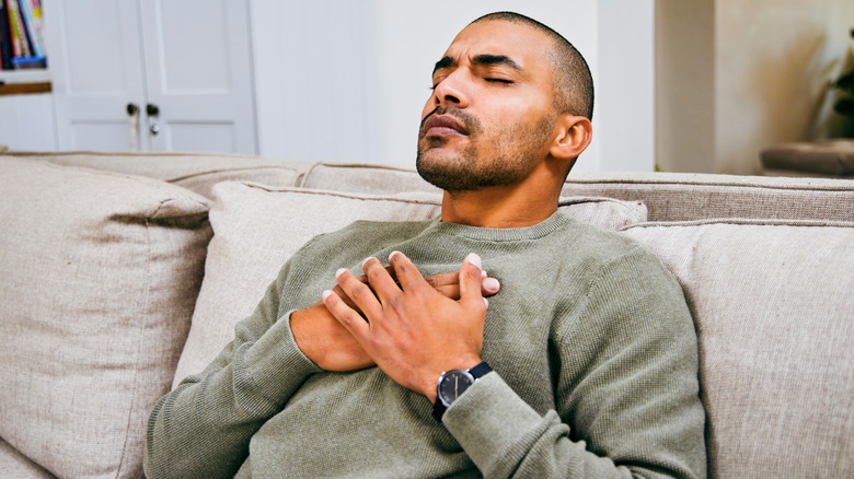 Man sitting on couch clutching chest