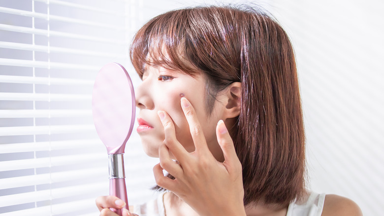 woman looking at skin in mirror