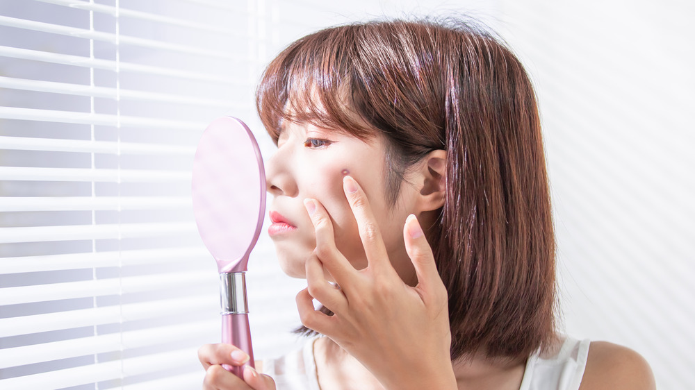 woman looking at skin in mirror