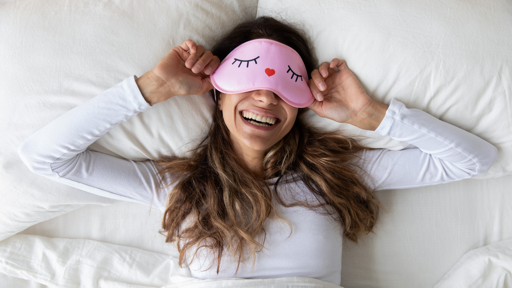 Woman waking up with eye mask on, smiling
