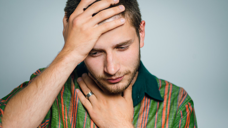 man with hand on forehead and throat