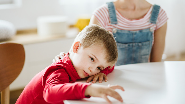 boy with head on a table not paying attention to his mom