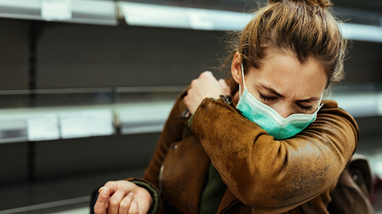 Masked woman coughing into sleeve