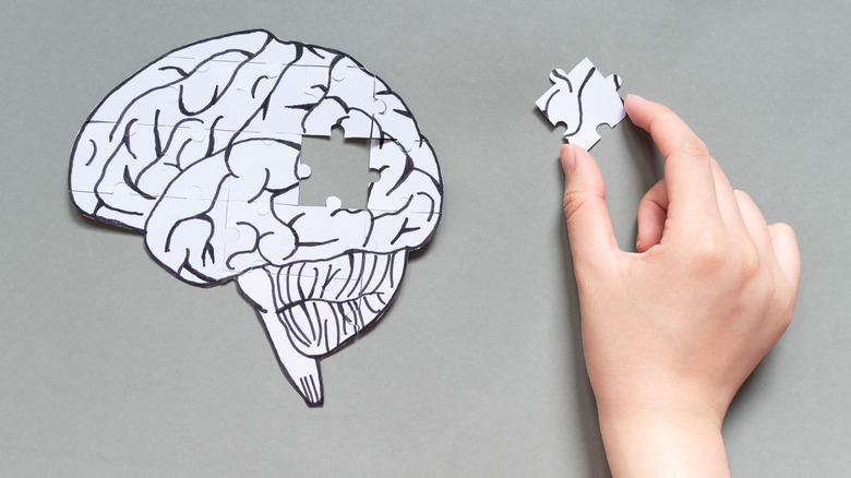 Puzzle of a brain missing a puzzle piece which is being held by a hand